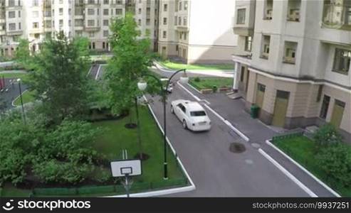 Aerial shot of green yard of multistorey houses with playground and two cars driving