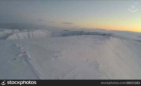 Aerial shot of snowy mountains with view to the winter resort in the distance. Arctic scene of Khibins in the evening, Russia