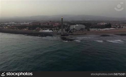 Aerial shot of the Gran Canaria resort and Maspalomas Lighthouse in the evening. Flying from the ocean to the beach