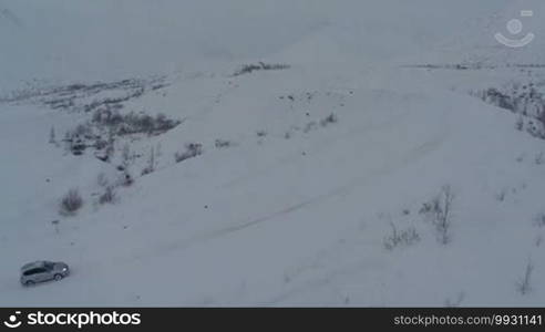 Aerial view of a car getting through the heavy deep snow on mountain road on dull winter day