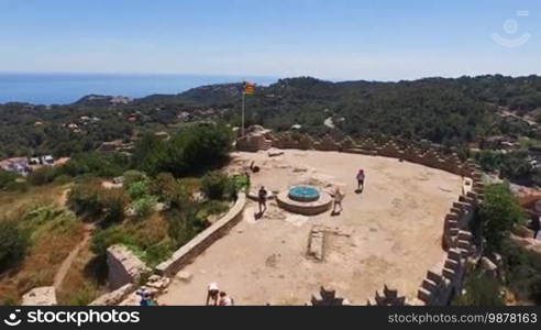 Aerial view of an old architectural building with tourists on the castle. The national flag is waving on the castle. Spain, Catalonia, Begur Castle