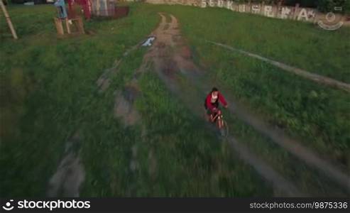 Aerial view of boy riding a bike along countryside road between agricultural fields in summer, Russia