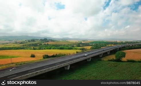 Aerial view of driving vehicles by the highway between yellow and green grass. Aerial view of fields and rural settlements by summer sunny day in Tuscany, Italy