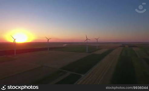 Aerial view of large wind turbines in a wind farm at sunset, producing sustainable and renewable energy.