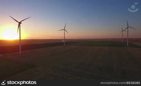 Aerial view of large wind turbines in a wind farm at sunset, producing sustainable and renewable energy.