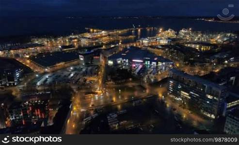 Aerial view of the night city with street lighting and moving traffic near the sea and ships in the port