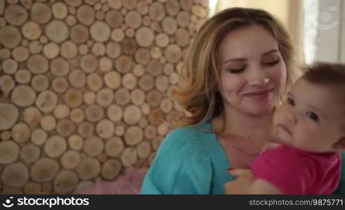 Affectionate young mother carrying her infant child and rocking her to sleep while dancing in the living room. Caring mother playing with her baby girl, spinning around and dancing in the domestic interior. Slow motion. Steadicam stabilized shot.