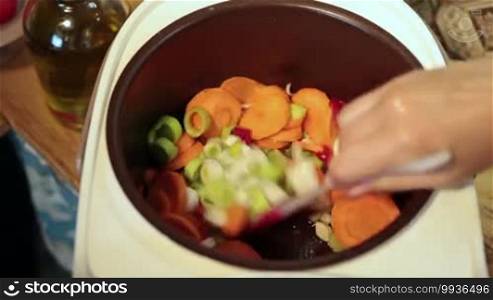 Angle view of woman hands stirring slowly vegetables in multicooker, while cooking soup in the kitchen