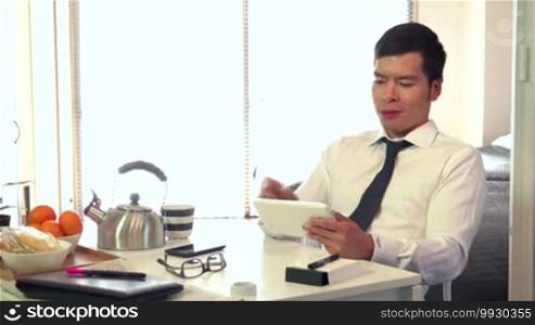 Asian people working at home with iPad, young business man at work with digital tablet computer and having breakfast in living room, portrait of happy businessman, busy male manager relaxing