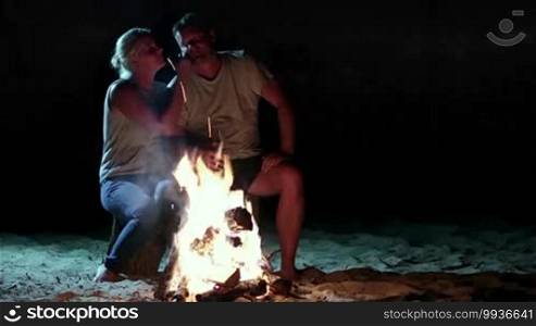 Attractive couple resting near bonfire at night. Couple relaxing near campfire. They gently hugging and kissing