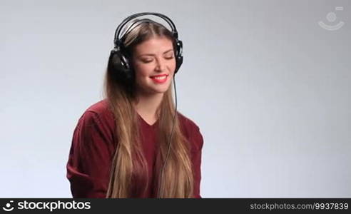 Attractive girl listening to the music in massive stylish headphones. Seductive brunette woman with red lipstick enjoying her favorite song on the radio, twisting her beautiful long hair around her finger, looking at the camera temptingly and alluringly.