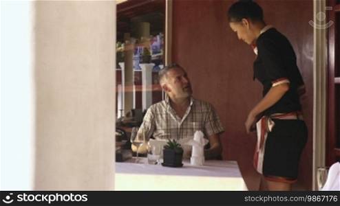 Attractive young Asian woman working as a waitress in an exclusive restaurant and attending to a customer. Dolly shot