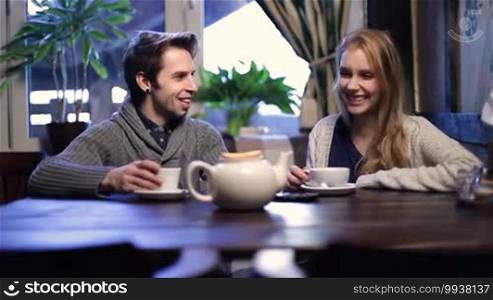 Attractive young couple having a great time together while relaxing in a cafe and talking. Cheerful teenagers spending leisure at a restaurant, chatting, drinking tea, and smiling.