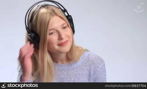 Attractive young woman in headphones enjoying music on white background. Happy teenage girl looking at camera silently saying what and laughing. Girl lifting one earcups with smile and nodding then putting earcup back on ear and continues listening.