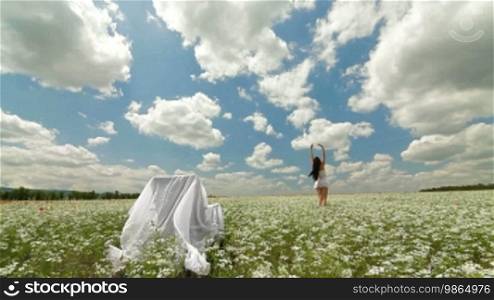 Attractive young woman relaxing in a white blossoming field with her arms spread widely