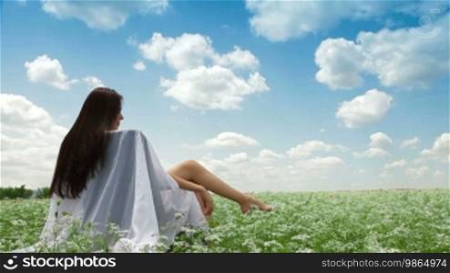 Attractive young woman sitting in a white blossoming field with her arms spread widely