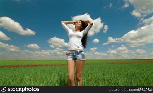 Attractive young woman standing in a green wheat field.