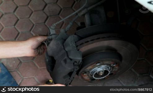 Auto mechanic working on brakes in a car repair shop.