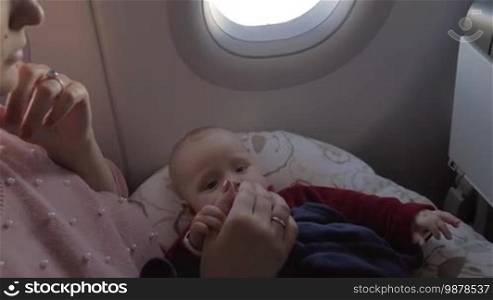 Baby girl traveling by plane with mum. Child lying on mother's lap and following her moving fingers