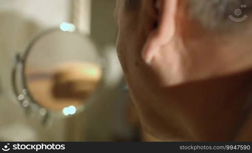 Back view of a mature man shaving in the bathroom with his reflection in a small round mirror