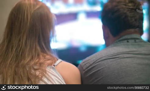 Back view of a young man and woman staring at a TV screen. Entertainment time or television addicts