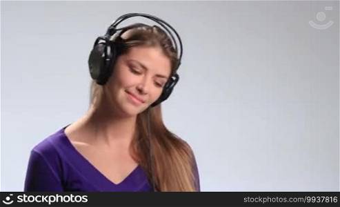 Beautiful brunette woman with headset listening to the upbeat music, swaying along with the rhythm, bobbing her head. Emotional girl enjoying music, opening her deep brown eyes and looking at the camera alluringly and teasingly.