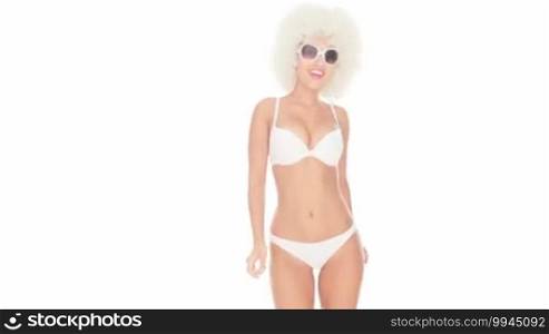 Beautiful sexy woman in a bikini and sunglasses and with a blond afro hairstyle dancing on a white studio background
