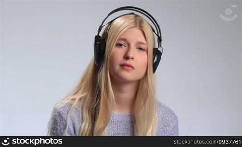 Beautiful teenager girl with sad facial expression listening to the song on radio on white background. Young disappointed woman in headphones swaying along with melancholic music and closing her eyes.