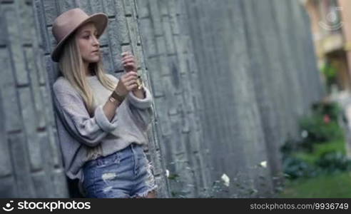 Beautiful woman smoking and leaning on the loft brick wall. Sexy blonde female smoking under stress and wanting to relax, letting out smoke cigarettes