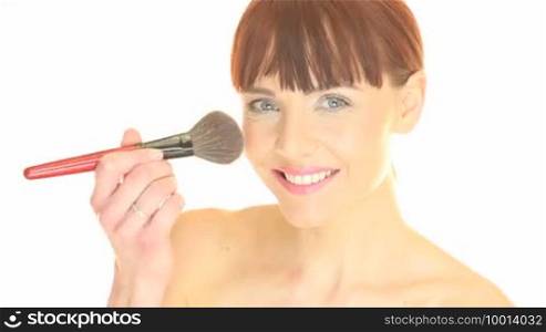 Beautiful woman using a large soft cosmetics brush to apply blusher to her cheek