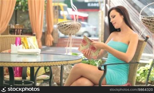 Beautiful young woman in a cocktail dress looking at the menu in the cafe