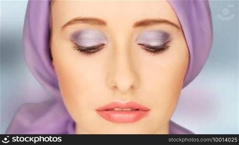 Beauty portrait of a woman with large blue-grey eyes wearing subtle makeup and a lilac headscarf