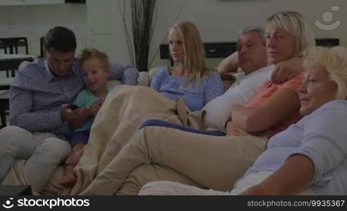 Big family relaxing at home. Parents, child, and grandparents watching TV. Father and son changing channels with remote