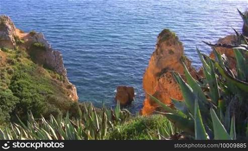 Blick auf Felsengebilde Stein im blauen Meer von einem grun bewachsenen Felsen die Sonne spiegelt sich im Wasser Kuste der Algarve Portugal