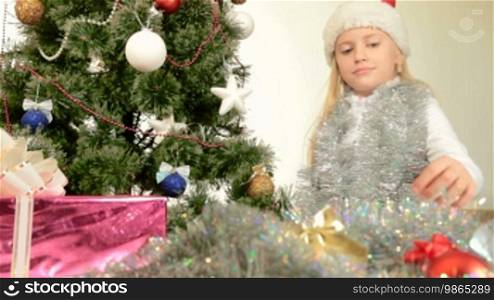 Blonde little girl decorating Christmas tree at home