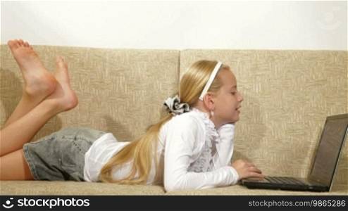 Blonde little girl listening to music on laptop at home