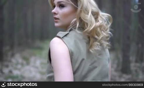 Blonde woman in the forest running, looking behind scared