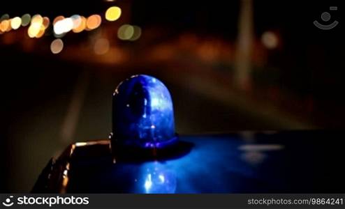 Blue emergency light on the roof of a police car riding down the street of the night city