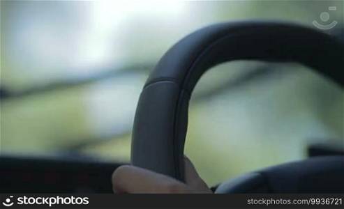 Blurred windshield wipers in action. Foreground woman driver holding steering wheel and driving. Background blurred windscreen wipers working. View inside out