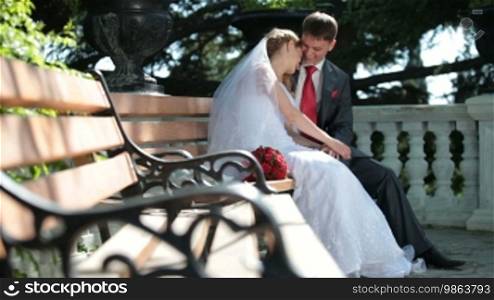 Bride and groom sit on a bench in the park