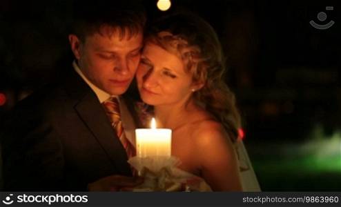 Bride and groom standing embraced at night, holding a burning candle in their hands