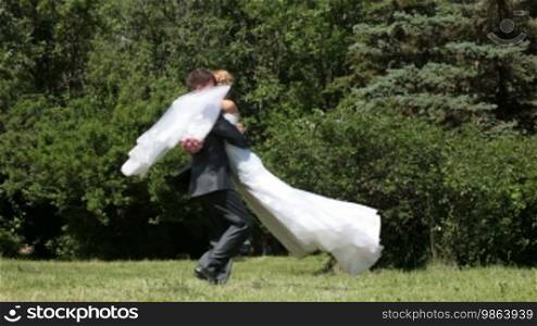 Bride spinning groom, holding her in his arms in the park
