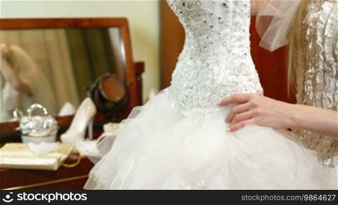 Bride trying on a wedding dress near the mirror with wedding accessories in the background