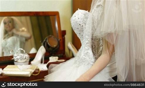Bride trying on a wedding dress near the mirror with wedding accessories in the background