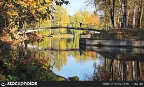 Bridge across lake in beautiful autumn city park, on it far away man with dog