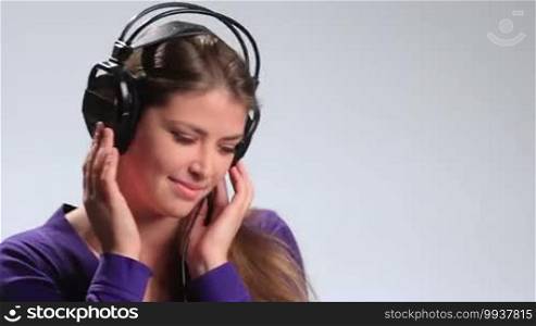 Bright positive teenage girl holding her headphones with both hands and enjoying the sound of music on white. Attractive young woman having fun, flirting with the camera playfully, making seductive looks while listening to the music in earphones.