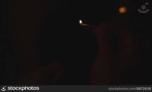 Burning match in man's hand on black background