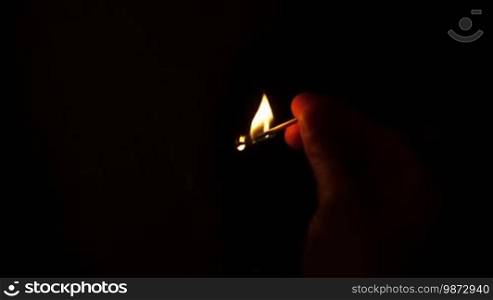Burning match in man's hand on black background