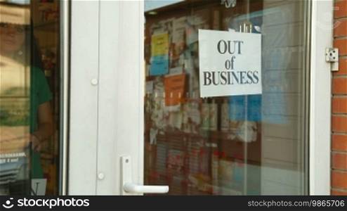 Business owner puts up "Out Of Business" sign on door of her store, medium shot