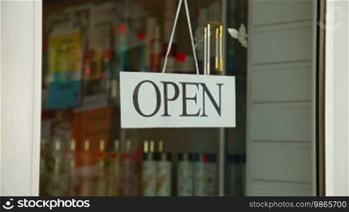 Business owner turns sign from open to closed in front of her store, medium shot